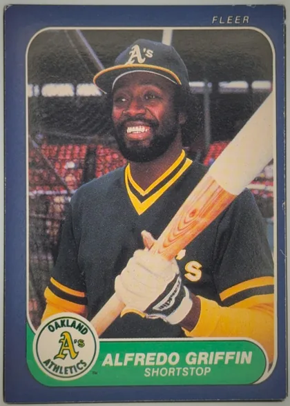 Front of 1986 Fleer Alfredo Griffin #417, front of a Fleer baseball card. A dark blue border surrounds a color action/portrait photograph of a smiling Black player wearing an Oakland…
