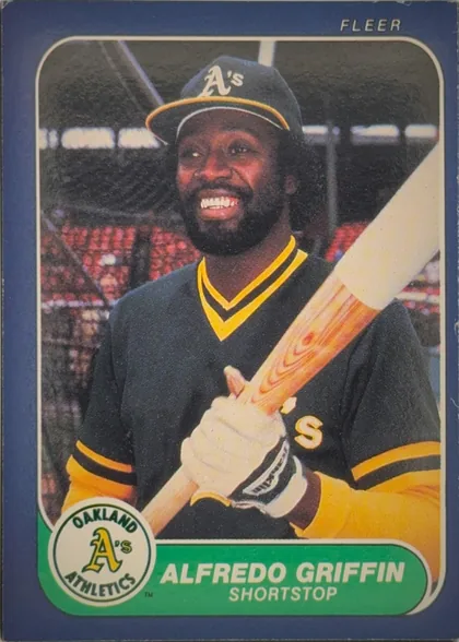 Front of 1986 Fleer Baseball Cards Alfredo Griffin #417 Base, front of a baseball card. A blue border surrounds a central color photograph of a smiling Black player with a beard, wearing a dark Oakland…