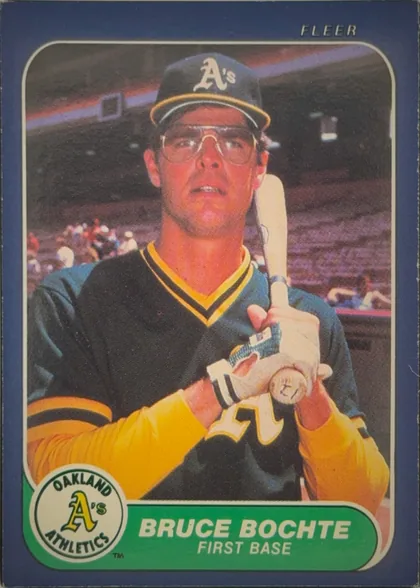 Front of 1986 Fleer Baseball Cards Bruce Bochte #413 Base, portrait baseball card front. A player in an Oakland Athletics uniform and batting helmet is shown holding a bat. The photograph is framed by a…