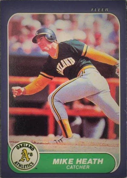Front of 1986 Fleer Baseball Cards Mike Heath #418 Base, portrait baseball card front. A large color action photograph shows a player in an Oakland uniform sliding or running near home plate. FLEER appears…