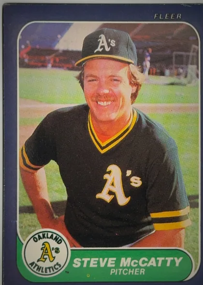 Front of 1986 Fleer Baseball Cards Steve McCatty #427 Base, front of a Fleer baseball card. A navy border surrounds a rounded-corner action/portrait photograph of a smiling player in an Oakland Athletics cap…