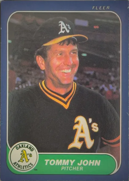 Front of 1986 Fleer Baseball Cards TOMMY JOHN #422 Base, upright portrait baseball card showing Tommy John in an Oakland Athletics uniform and cap, smiling in front of a stadium crowd. A large Oakland A's…