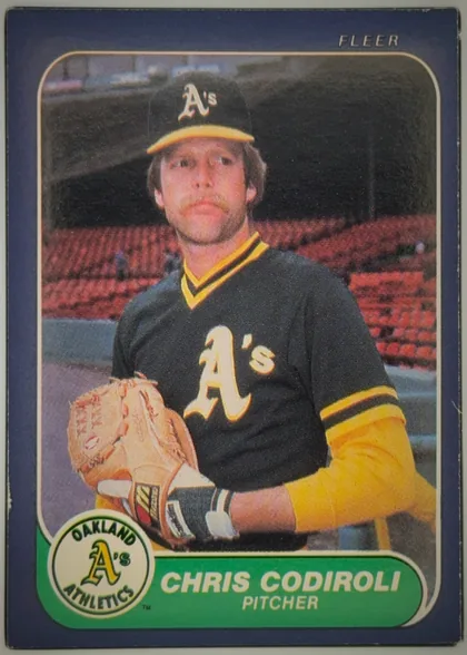 Front of 1986 Fleer Chris Codiroli #414 Base, front of a Fleer baseball card. A navy-blue border frames a rounded-corner color photograph of a pitcher wearing a black Oakland Athletics jersey…