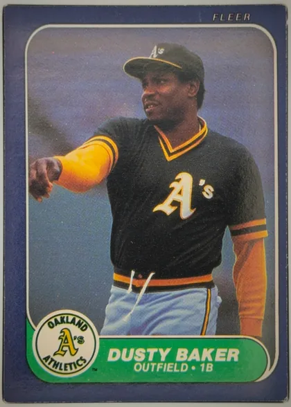 Front of 1986 Fleer DUSTY BAKER #411 Base, portrait-oriented baseball card front. A player in an Oakland Athletics uniform is shown in a large color photograph, extending one arm. The card…