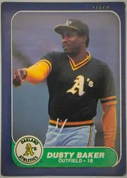 Front of 1986 Fleer Dusty Baker #411 Base, front of a Fleer baseball card. A full-color action photograph of a player in a black Oakland Athletics home jersey with yellow-and-black trim, a…