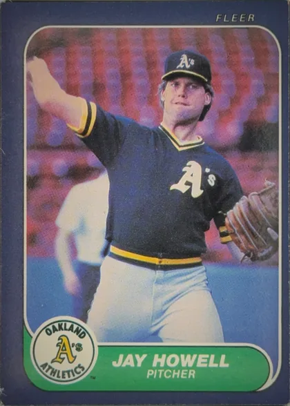 Front of 1986 Fleer Jay Howell #421 Base, front of a baseball card. A dark blue/purple border surrounds a color action photograph of a pitcher in a dark navy Oakland Athletics uniform with…