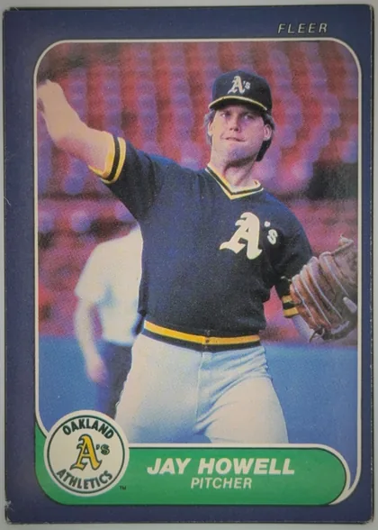 Front of 1986 Fleer Jay Howell #421 Base, front of a Fleer baseball card. A dark blue/purple border surrounds a rounded-corner color action photograph of a pitcher in a navy Oakland…