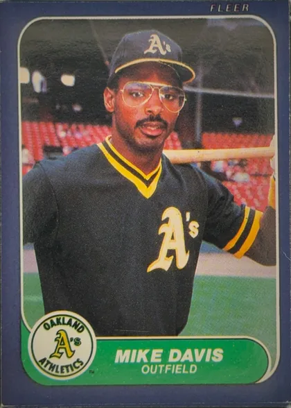 Front of 1986 Fleer Mike Davis #416 Base, front of a baseball card. A color action/portrait photograph fills most of the card, showing a player in a dark Oakland Athletics jersey with a…