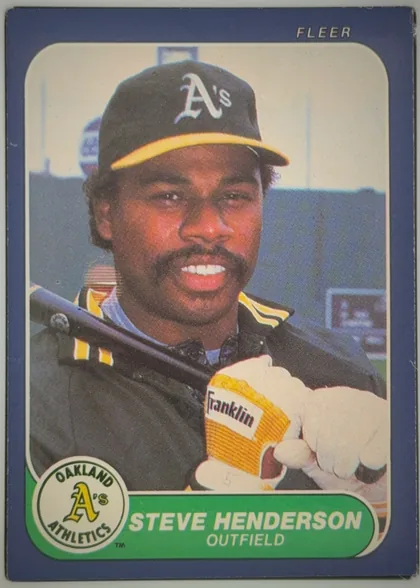 Front of 1986 Fleer Steve Henderson #419 Base, front of a Fleer baseball card. A dark blue border surrounds a rounded-corner color photograph of a smiling Black man wearing a dark Oakland…