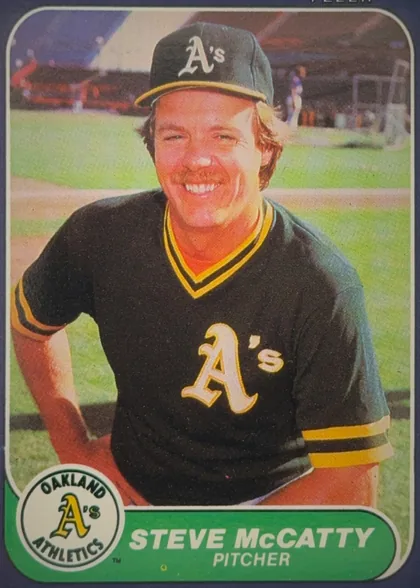 Front of 1986 Fleer Steve McCatty #427 Base, upright portrait-oriented baseball card front. A smiling Oakland Athletics player in a black-and-gold uniform and cap fills the photograph, with a…