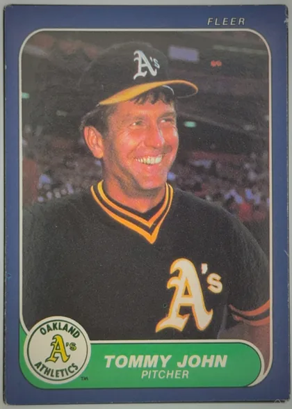 Front of 1986 Fleer Tommy John #422, upright portrait-format baseball card front. A color photograph shows Tommy John in an Oakland Athletics uniform and cap, centered against a stadium…