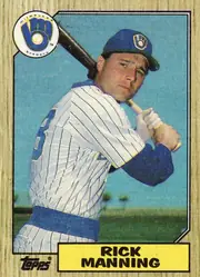 Front of 1987 Topps Baseball RICK MANNING #706 Base, portrait-oriented baseball card front. A Milwaukee Brewers player is shown batting in a white pinstriped uniform and blue cap against a blue-green…