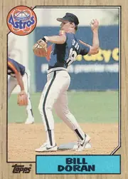 Front of 1987 Topps Bill Doran #472 1987 Topps Base, portrait baseball card front showing a Houston Astros player in a blue uniform pitching on a baseball field. The circular Astros logo overlaps the…