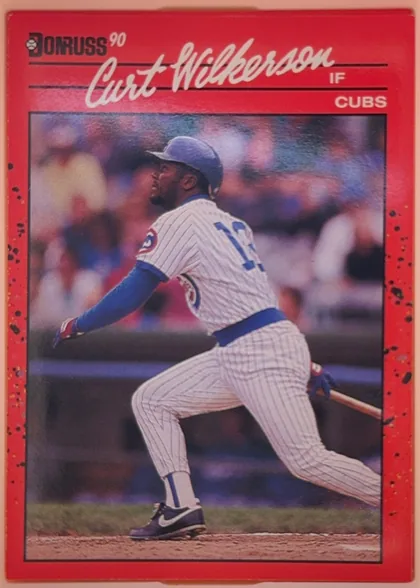 Front of 1990 Donruss Baseball Curt Wilkerson #608, portrait-oriented baseball card front. A red speckled border surrounds a large action photograph of a Chicago Cubs player in a white pinstriped…