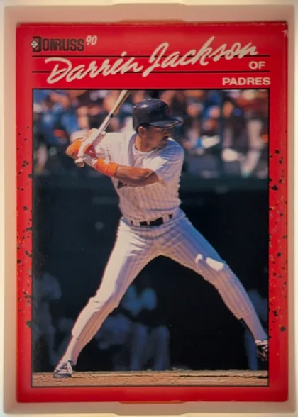 Front of 1990 Donruss Baseball Darren Jackson #641, portrait baseball card front. A red border surrounds a color action photograph of a batter in a white pinstriped uniform swinging a bat. The upper…