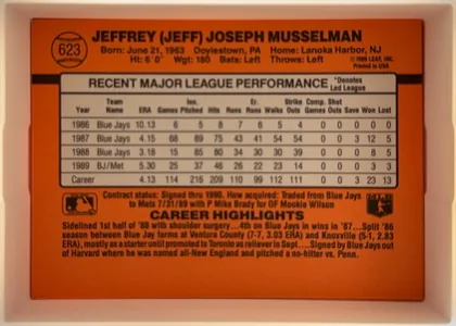 Back of 1990 Donruss Baseball Jeff Musselman #623, upright landscape-oriented card back dominated by an orange-red field. The upper section shows a baseball-shaped number emblem at left, the player's…