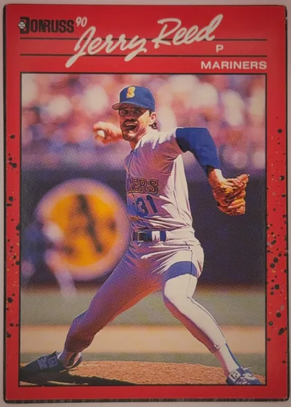 Front of 1990 Donruss Baseball Jerry Reed #614, portrait baseball card front. A red border surrounds a large action photograph of a Mariners pitcher in a blue-and-white uniform delivering a pitch…