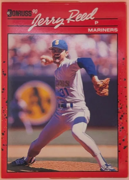 Front of 1990 Donruss Baseball Jerry Reed #614, portrait baseball card front. A red speckled border surrounds a large action photograph of a pitcher in a Mariners uniform. The upper portion has a…