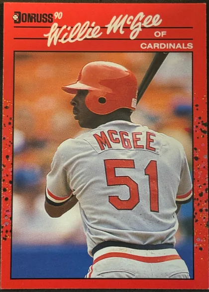 Front of 1990 Donruss Baseball Willie McGee #632, portrait-format baseball card front. A red speckled border surrounds a large action photograph of Willie McGee seen from behind in a Cardinals…