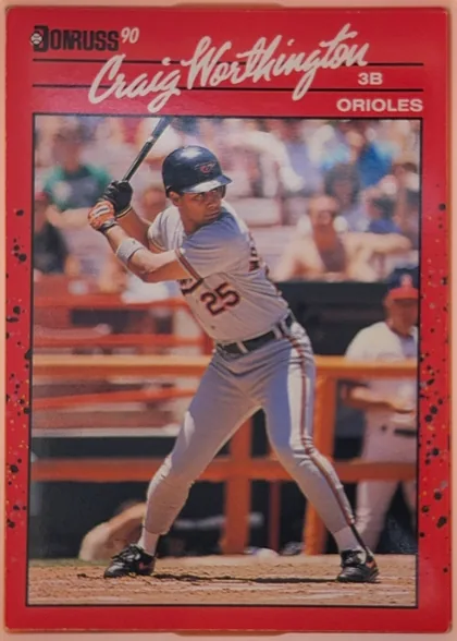 Front of 1990 Donruss Craig Worthington #141, portrait-oriented baseball card front. A red header and border surround a large action photograph of Craig Worthington batting. The upper left has…