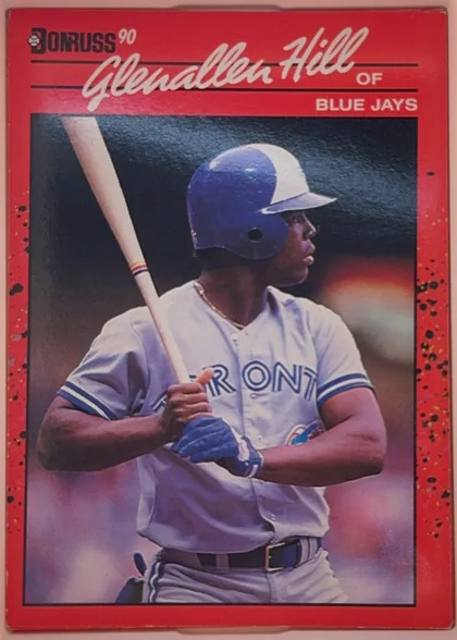 Front of 1990 Donruss Glenallen Hill #627, portrait baseball card front. A red speckled border surrounds a large action photograph of Glenallen Hill batting in a Blue Jays uniform. The…