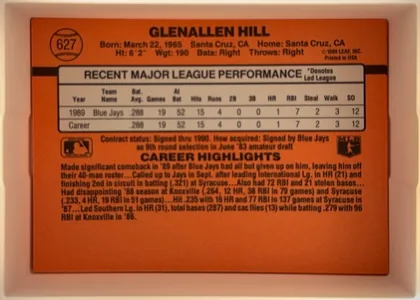 Back of 1990 Donruss Glenallen Hill #627, upright horizontal baseball card back dominated by an orange-red background. The upper area contains a baseball-shaped number graphic at left, the…