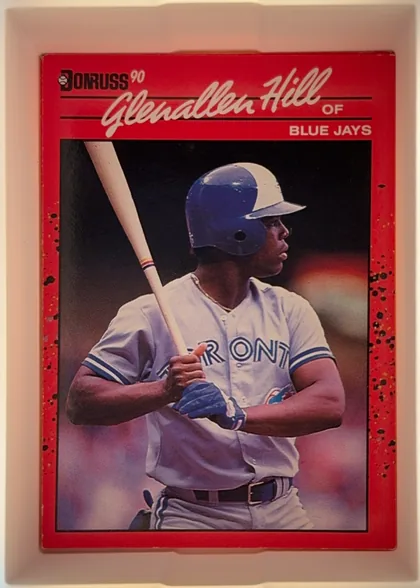 Front of 1990 Donruss Glenallen Hill #627, upright portrait baseball card front. A red header and border surround a color photograph of a batter in a Toronto Blue Jays uniform holding a bat…
