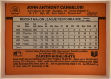 Back of 1990 Donruss John Cangelosi #565, landscape-oriented baseball card back. A solid orange field fills the card. At upper left is a baseball-stitch circle containing the number 565…