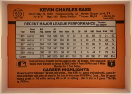 Back of 1990 Donruss Kevin Bass #589, upright landscape-format card back dominated by an orange background. The player name is centered across the top, with a baseball-shaped number…