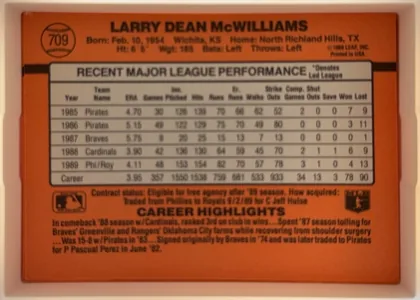 Back of 1990 Donruss Larry McWilliams #709, landscape-oriented baseball card back with an orange-red field. A circular baseball graphic containing card number 709 appears at the upper left…