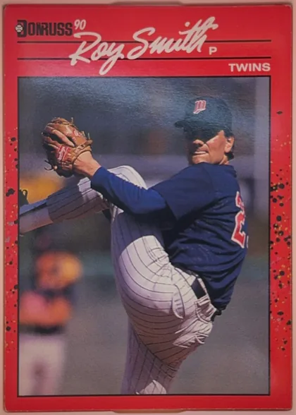 Front of 1990 Donruss Roy Smith #273, portrait baseball card front. A red, heavily speckled border surrounds a large action photograph of a pitcher in a Minnesota Twins uniform. At the…