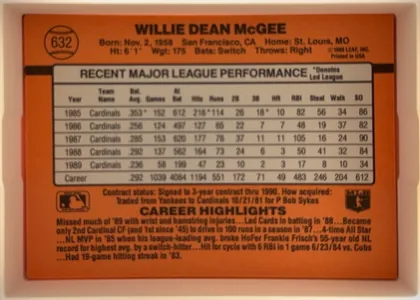 Back of 1990 Donruss Willie McGee #632, upright landscape-oriented baseball card back. The orange-red design has a black horizontal stripe across the upper-middle area. A baseball-shaped…