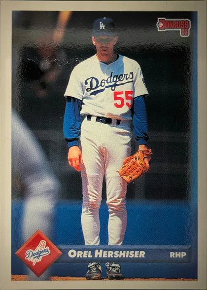 Front of 1992 Donruss Orel Hershiser #247 1992 Donruss #247 (base, Series One), portrait baseball card front. A full-body photograph shows a pitcher standing facing forward in a white Los Angeles Dodgers home uniform with blue…