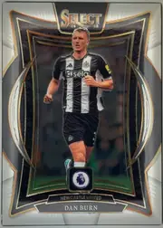 Front of 2024-25 Panini Select Premier League Soccer Dan Burn #87 Terrace, upright portrait soccer card front. A Newcastle United player in a black-and-white kit is shown running centrally within an ornate dark frame. The…