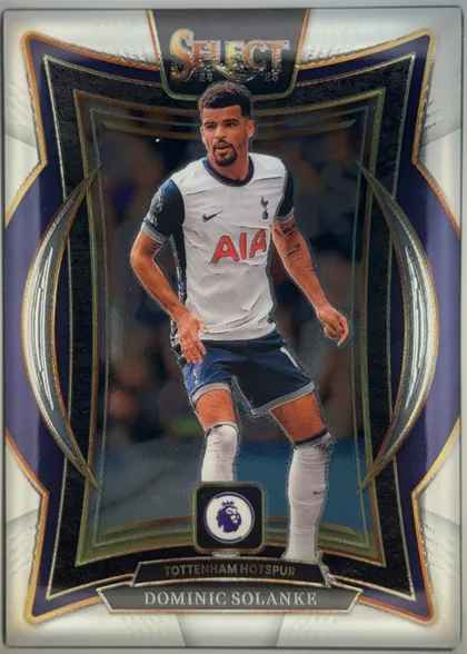 Front of 2024-25 Panini Select Premier League Soccer Dominic Solanke #6, upright portrait soccer card. A full-body image of Dominic Solanke in a white Tottenham Hotspur kit is centered within an ornate dark navy and black…