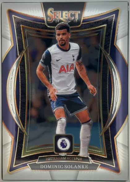 Front of 2024-25 Panini Select Premier League Soccer Dominic Solanke #6 White Ice Prizm /85, upright portrait soccer card featuring Dominic Solanke in a white Tottenham Hotspur jersey, centered in an ornate dark navy, black, gold, and silver…