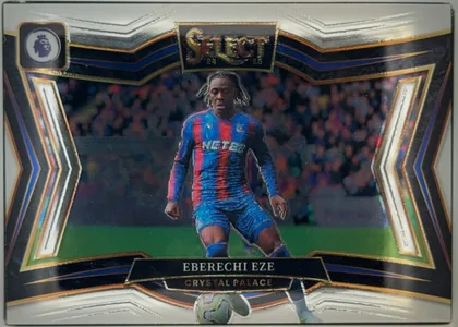 Front of 2024-25 Panini Select Premier League Soccer EBERECHI EZE #215 Field Level, front of a landscape soccer card. A Crystal Palace player with braided hair is shown roughly knees-up in the blue-and-red striped NET82 home kit…