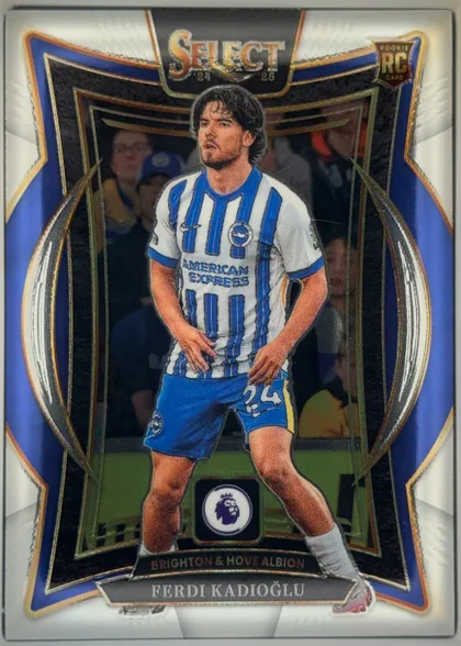 Front of 2024-25 Panini Select Premier League Soccer Ferdi Kadioglu #36 Terrace, upright portrait soccer card front. A player in Brighton & Hove Albion's blue-and-white striped kit stands in the center against a stadium…