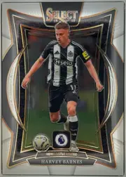 Front of 2024-25 Panini Select Premier League Soccer Harvey Barnes #89, upright portrait soccer card. A male footballer in a black-and-white Newcastle United kit is pictured running with a ball. The top has a large…