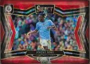 Front of 2024-25 Panini Select Premier League Soccer JÉRÉMY DOKU #222 Field Level Prizm, front of a landscape-format soccer card with a red, black, gold, and blue geometric foil design. A Manchester City player in a light blue kit is…