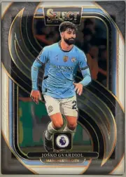 Front of 2024-25 Panini Select Premier League Soccer JOŠKO GVARDIOL #154 Mezzanine, portrait football card front. A full-body image of Josko Gvardiol in a light blue Manchester City kit is centered within an ornate black, blue, and…