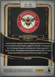 Back of 2024-25 Panini Select Premier League Soccer Mathias Jensen #103 Mezzanine Prizm, upright portrait-oriented card back. A black-and-gold decorative design fills most of the surface, with red, gold, and white border accents. The top…