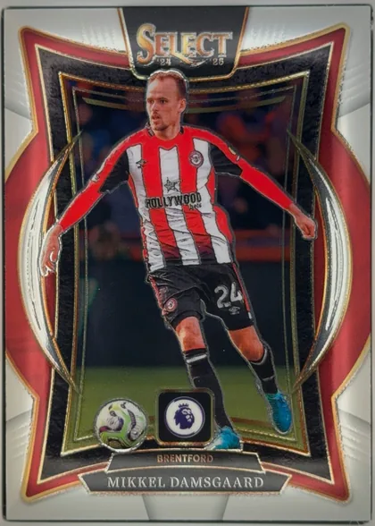 Front of 2024-25 Panini Select Premier League Soccer Mikkel Damsgaard #4 Terrace, upright portrait soccer card front. A Brentford player in a red-and-white striped kit is centered against a dark stadium background. The SELECT 24…