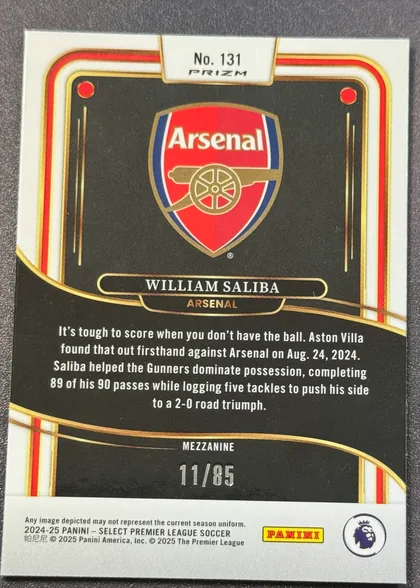 Back of 2024-25 Panini Select Premier League Soccer William Saliba #131 Mezzanine /85, serial numbered 11/85, upright landscape-oriented card back with a white border and ornate red, gold, and black curved framing. The upper center has a white tab reading…