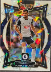 Front of 2024 Panini Select Premier League Dominic Solanke #6 Terrace Prizm /85, serial numbered 28/85, front-facing portrait football card. A full-body image of Dominic Solanke in a white Tottenham Hotspur kit is centered over an abstract dark…