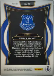 Back of 2024 Panini Select Premier League Iliman Ndiaye #58 Base Set Premier League Terrace, portrait-oriented card back. A white border surrounds a blue, black, gold, and cream ornamental frame. The Everton crest is centered in the upper…