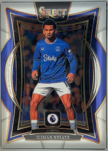 Front of 2024 Panini Select Premier League Iliman Ndiaye #58 Base Set Premier League Terrace, portrait-oriented football card front. A player in an Everton blue kit is centered within an ornate black, blue, gold, and silver geometric frame…
