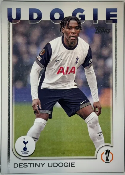 Front of 2024 Topps UEFA Destiny Udogie #71 Base, portrait soccer card front. A Tottenham Hotspur player in a white shirt with navy sleeves and red AIA sponsor stands on a soccer pitch. The large…