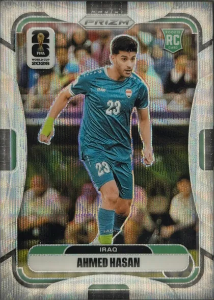 Front of 2026 Panini Prizm FIFA Ahmed Hasan #459, upright portrait soccer card front. A young player in a teal Iraq kit with number 23 is shown running in a stadium. The PRIZM logo is centered at…