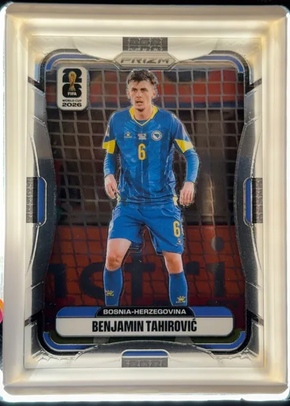 Front of 2026 Panini Prizm FIFA Benjamin Tahirovic #472 Base, portrait-format soccer card front. A full-body image of Benjamin Tahirovic in a blue Bosnia-Herzegovina kit stands in front of a soccer goal net…